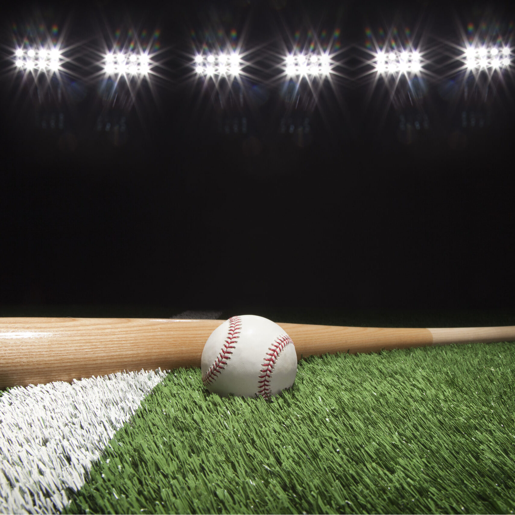 Baseball and bat at night under stadium lights on grass field with white stripe
